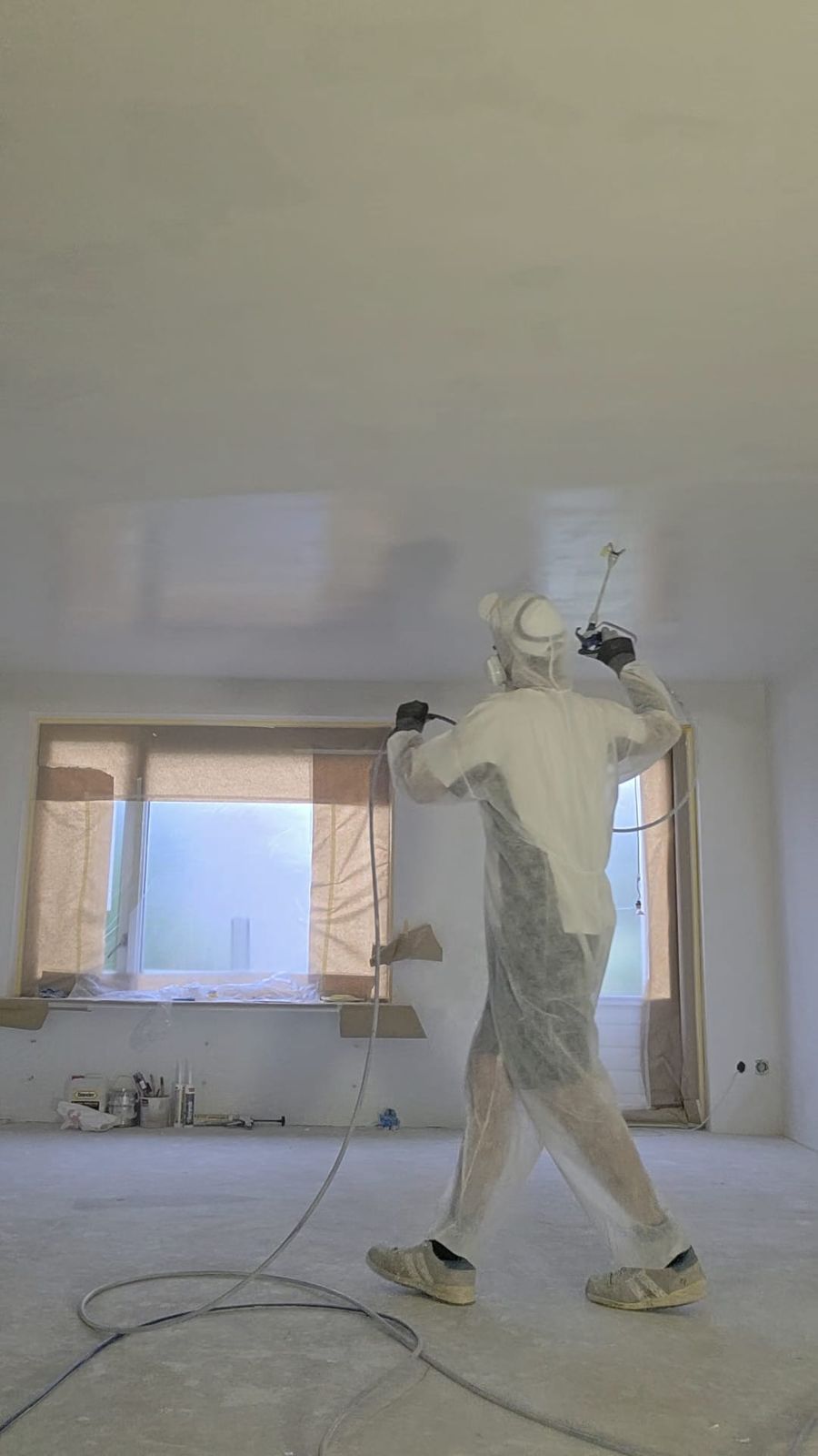 Stukadoor in wit beschermpak spuit het plafond met de sauspomp
