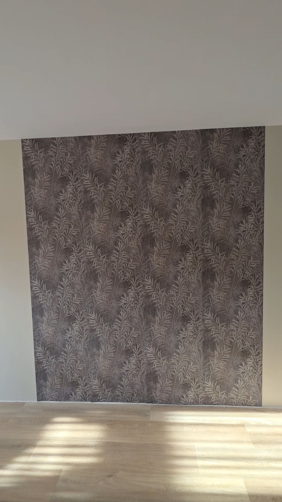 Accentwand met behang met een patroon van grassen en bladeren boven een lichte houten vloer